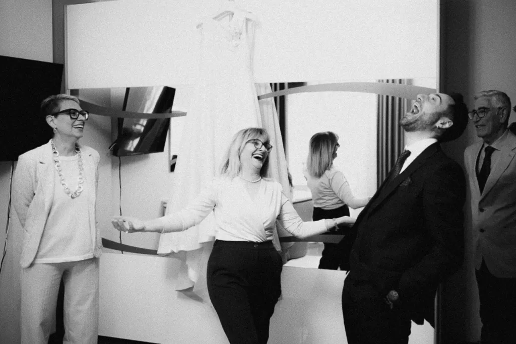 Sposo e suocera che ridono mentre la sposa si sta truccando. Come organizzare i tempi del matrimonio (dal mio punto di vista di fotografo)